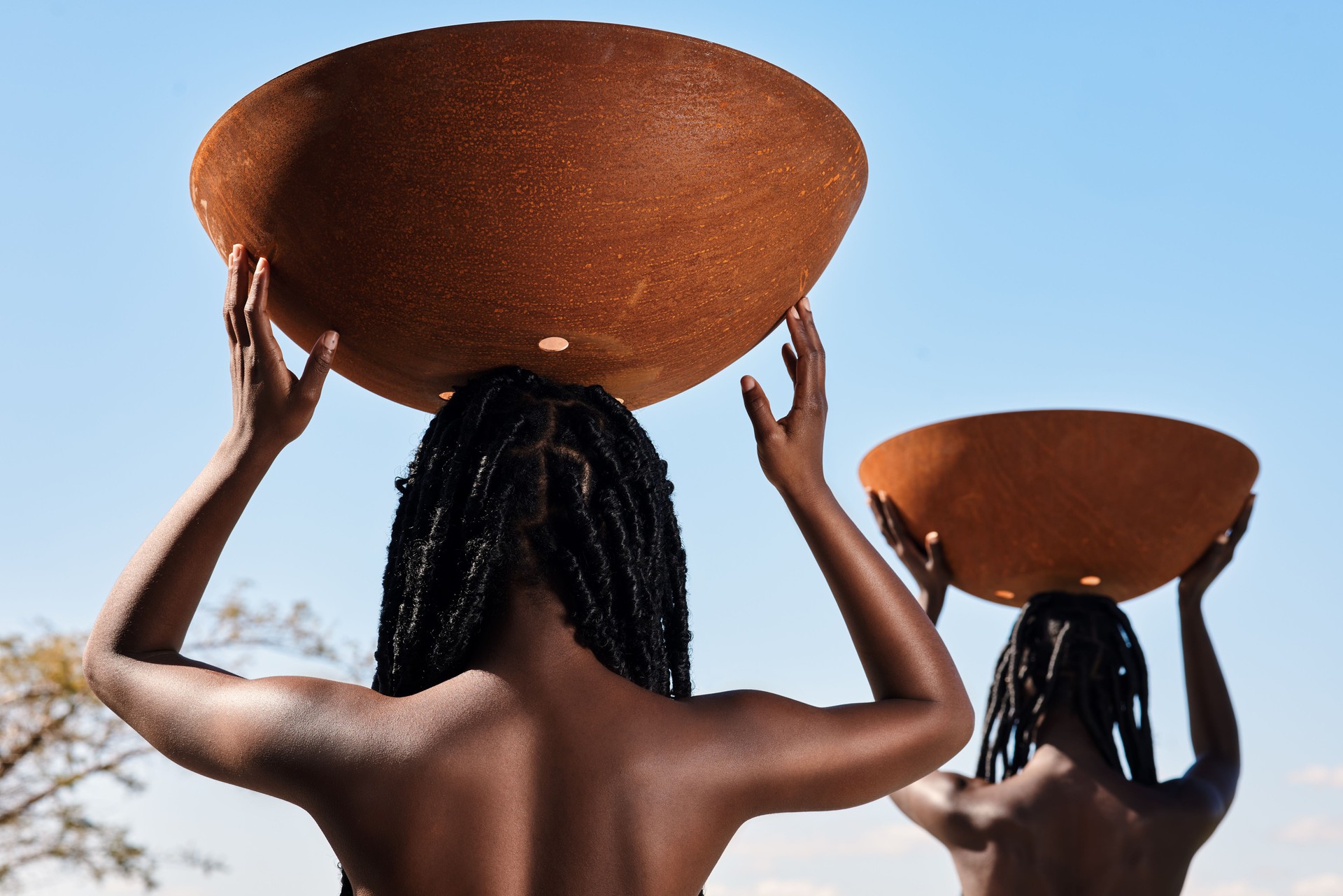 Rearview shot of two unrecognizable young women carrying pots on their heads outside